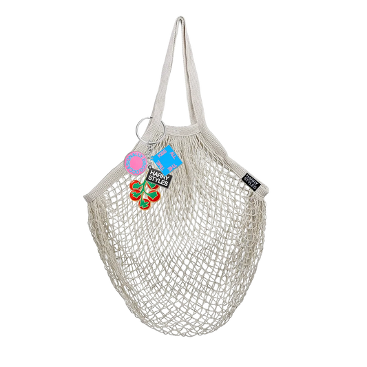 Natural cotton mesh grocery bag from Harry Styles merchandise featuring tomato keychain charms and collectible branded tags attached to handle ring
